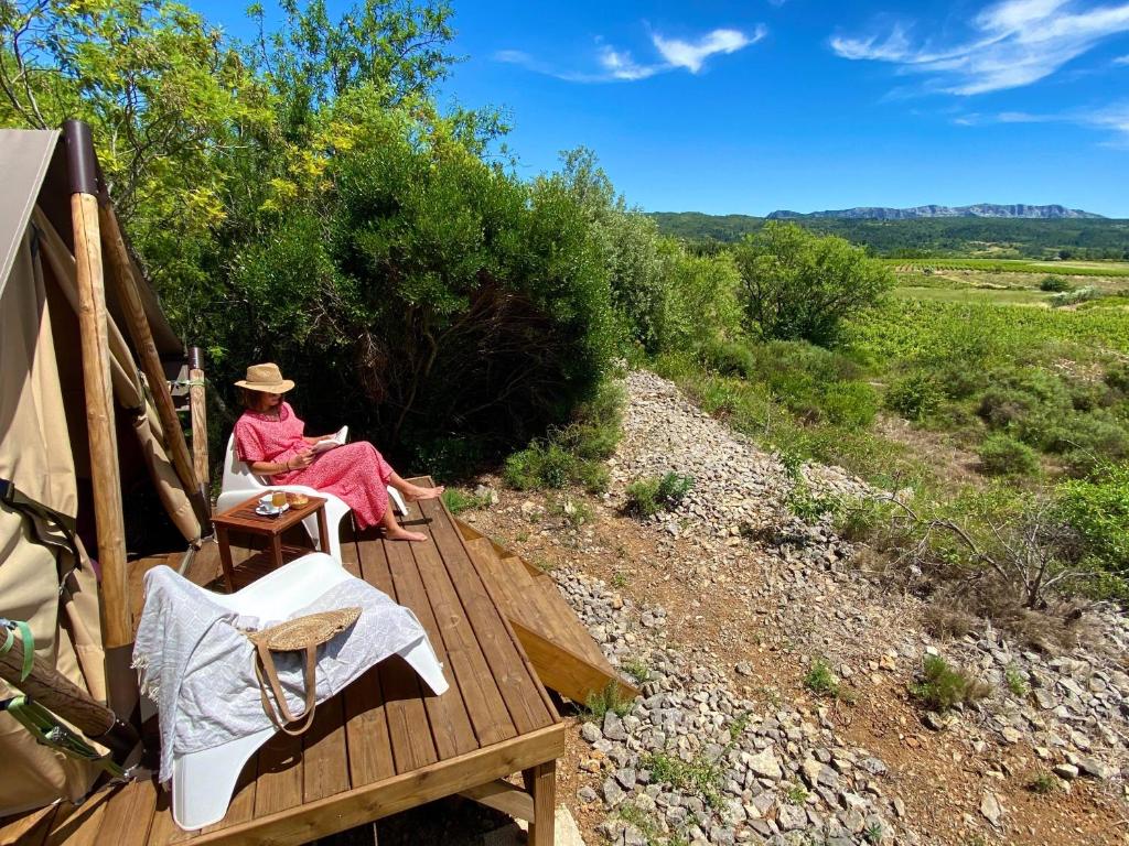 una mujer sentada en una terraza de madera leyendo un libro en Lodge en Pays Cathare en Tuchan