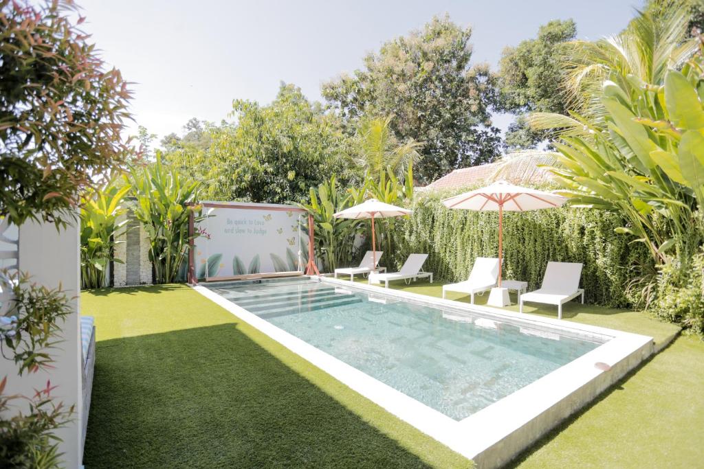 a pool with chairs and umbrellas in a yard at Gatsby Hotel Hostel in Uluwatu