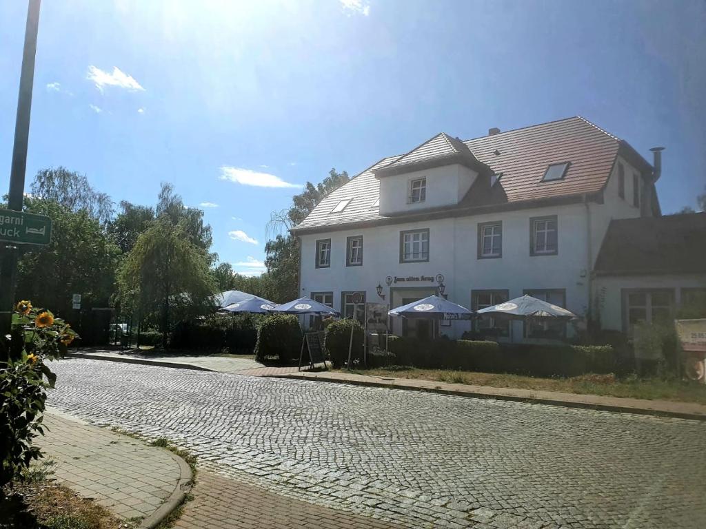 ein großes weißes Haus mit Sonnenschirmen am Straßenrand in der Unterkunft Landgasthof Alter Krug Potsdam OT Marquardt in Potsdam