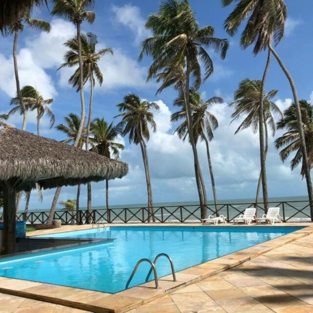 a swimming pool with palm trees and the ocean at Eco Paradise Cumbuco 131 in Cumbuco
