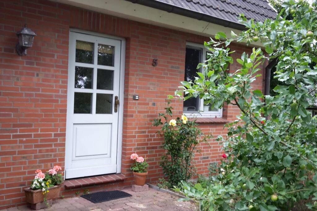 ein rotes Backsteinhaus mit einer weißen Tür und Blumen in der Unterkunft Ferienwohnung in Schleswig-Holstein, Hohn in Hohn