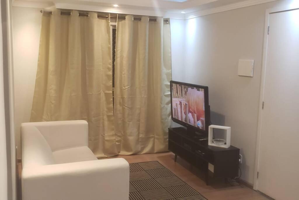 uma sala de estar com televisão e uma cadeira branca em Apto 2 quartos São José dos Pinhais Curitiba sem taxa de limpeza e próximo do aeroporto em São José dos Pinhais