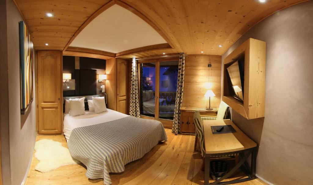a bedroom with a bed and a desk and a window at Hôtel Alpina &amp; SPA in Les Gets