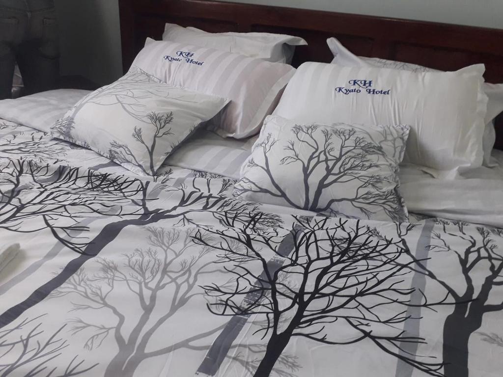 a bed with white comforter with trees on it at Kyato Hotel in Kasanda