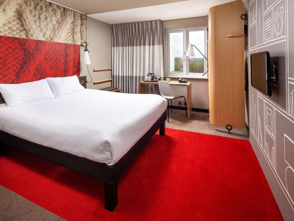 una habitación de hotel con una cama grande y una alfombra roja en ibis Rugby East, en Crick