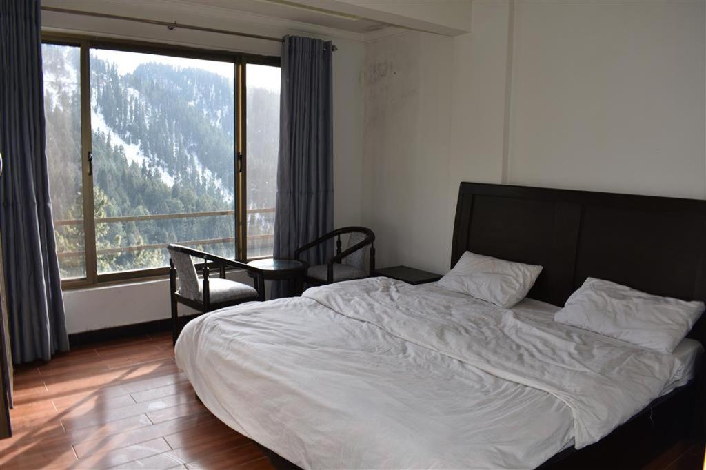 a bedroom with a large bed and a large window at Hotel Royal Inn in Murree