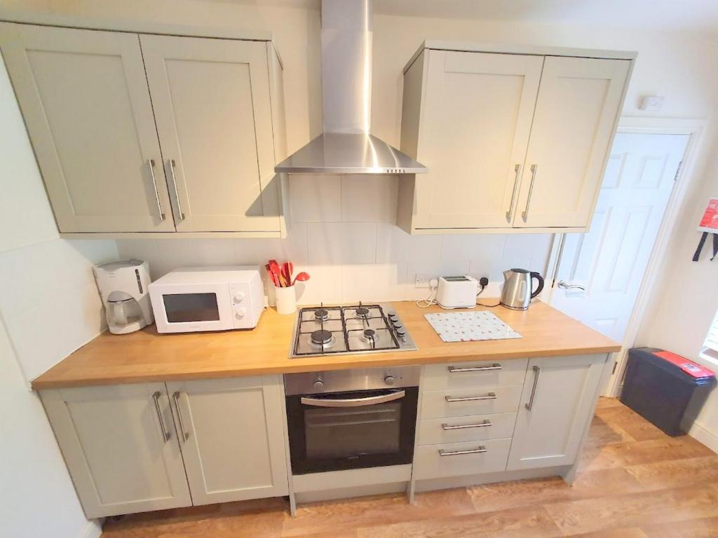 uma cozinha com armários brancos, um fogão e um micro-ondas em Bassett Flat with 2 Double Bedrooms and Superfast Wi-Fi em Sittingbourne