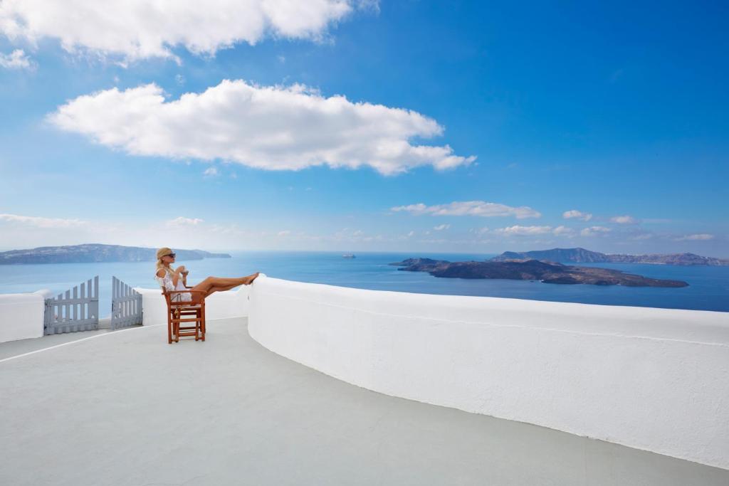 a woman sitting in a chair on a balcony looking out at the ocean at Volcano View by Caldera Collection in Fira