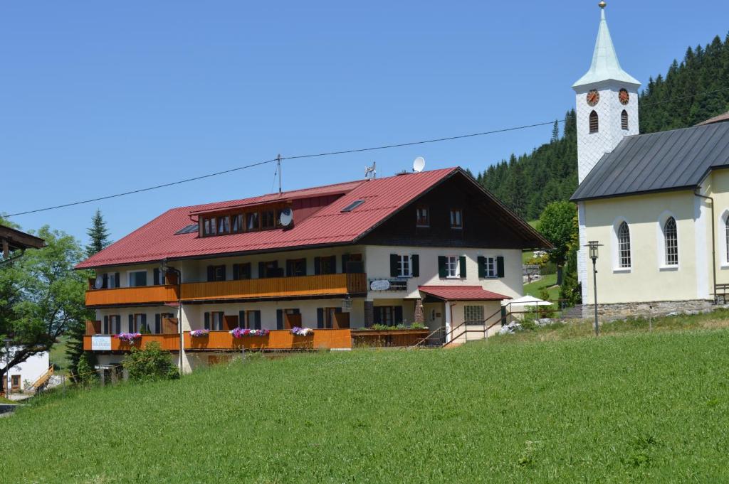 um edifício com um telhado vermelho ao lado de uma igreja em Bed & Breakfast Jungholz - Pension Katharina em Jungholz