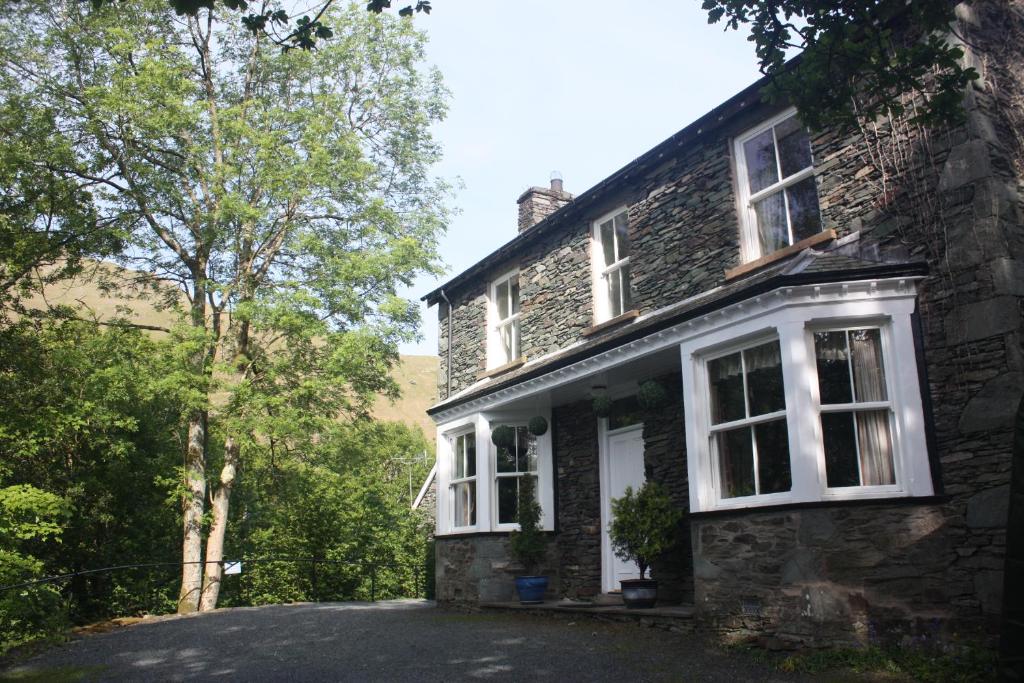 ein Steinhaus mit weißen Fenstern und einer Auffahrt in der Unterkunft Old Water View in Patterdale