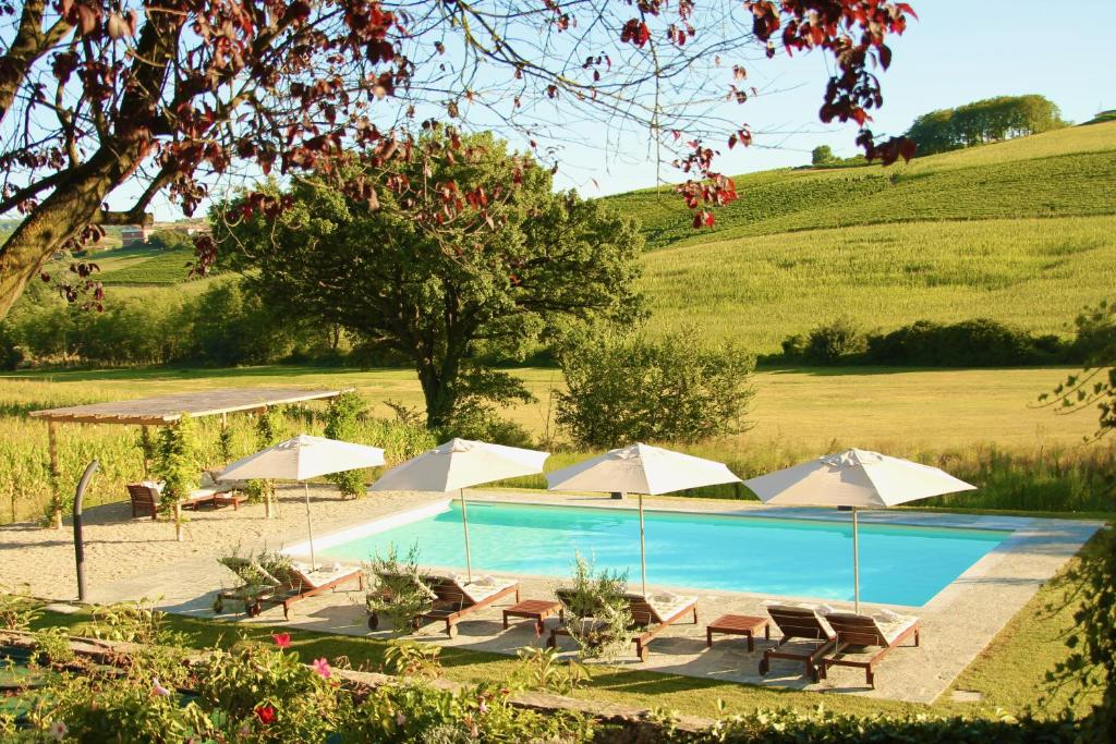 einen Pool mit Sonnenschirmen und Stühlen auf einem Feld in der Unterkunft Villa La Mura - Luxury Pool by the Vineyard in Costigliole dʼAsti