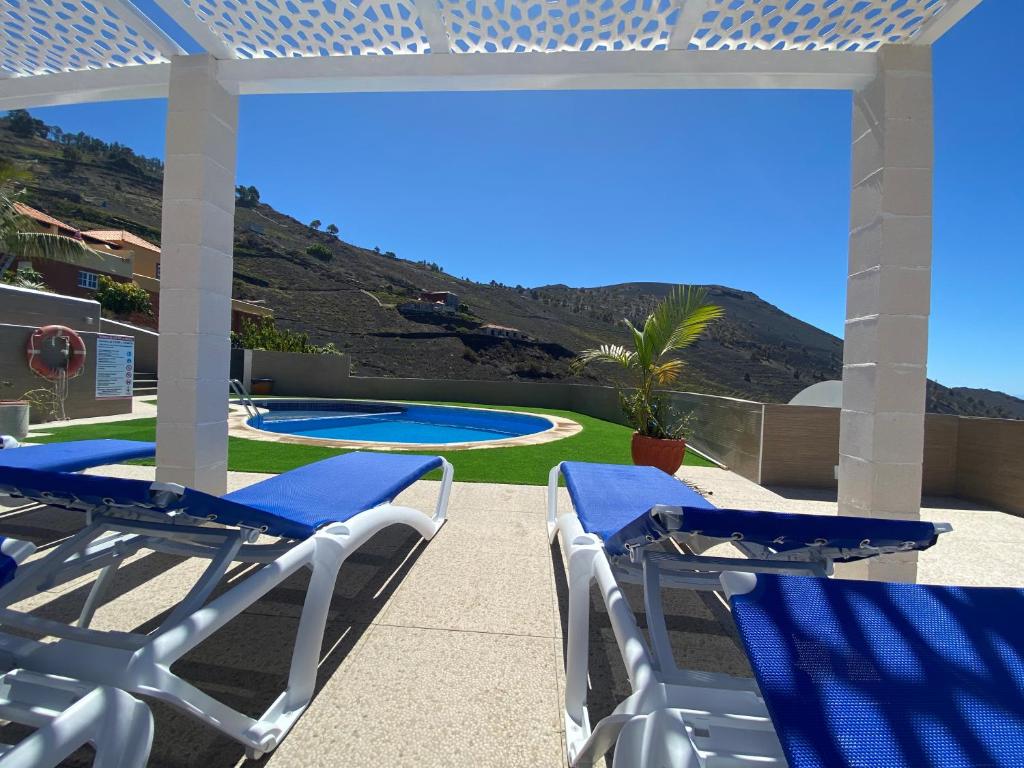 um pátio com cadeiras azuis e brancas e uma piscina em Apartamentos colon y bungalows em Los Quemados
