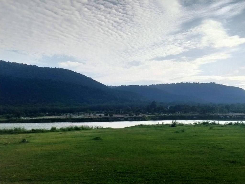 a green field with a lake and mountains in the background at Samerdrow Khao Yai in Mu Si