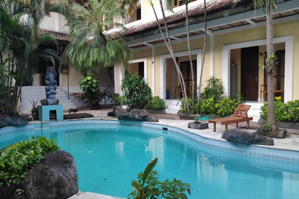 a swimming pool in front of a hotel with palm trees at Villa Puri Royan in Jimbaran