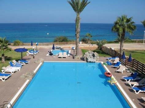 a swimming pool with chairs and umbrellas and the ocean at Fig Tree Bay Apartments in Protaras