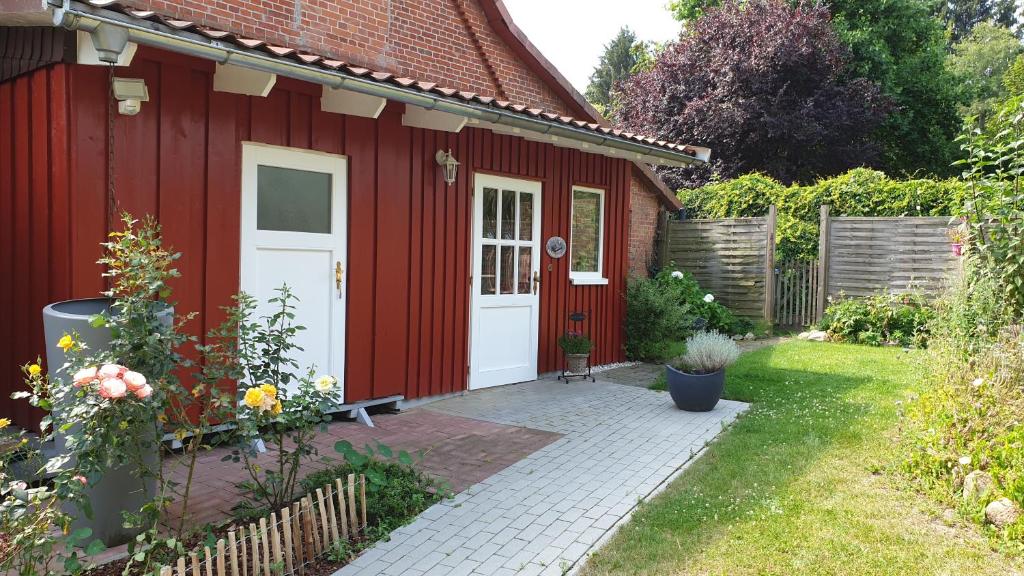 a red shed with a white door in a garden at Schnucken-Hus in Amelinghausen