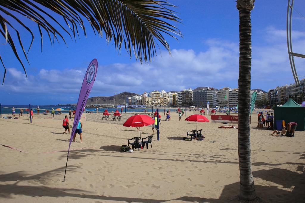 eine Gruppe von Menschen am Strand mit roten Sonnenschirmen in der Unterkunft Atlantic Apartments in Las Palmas de Gran Canaria