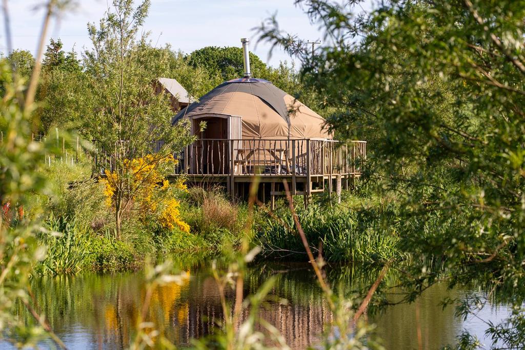 a round house with a deck on the side of a lake at Shepherd's Loch Glamping in Turriff