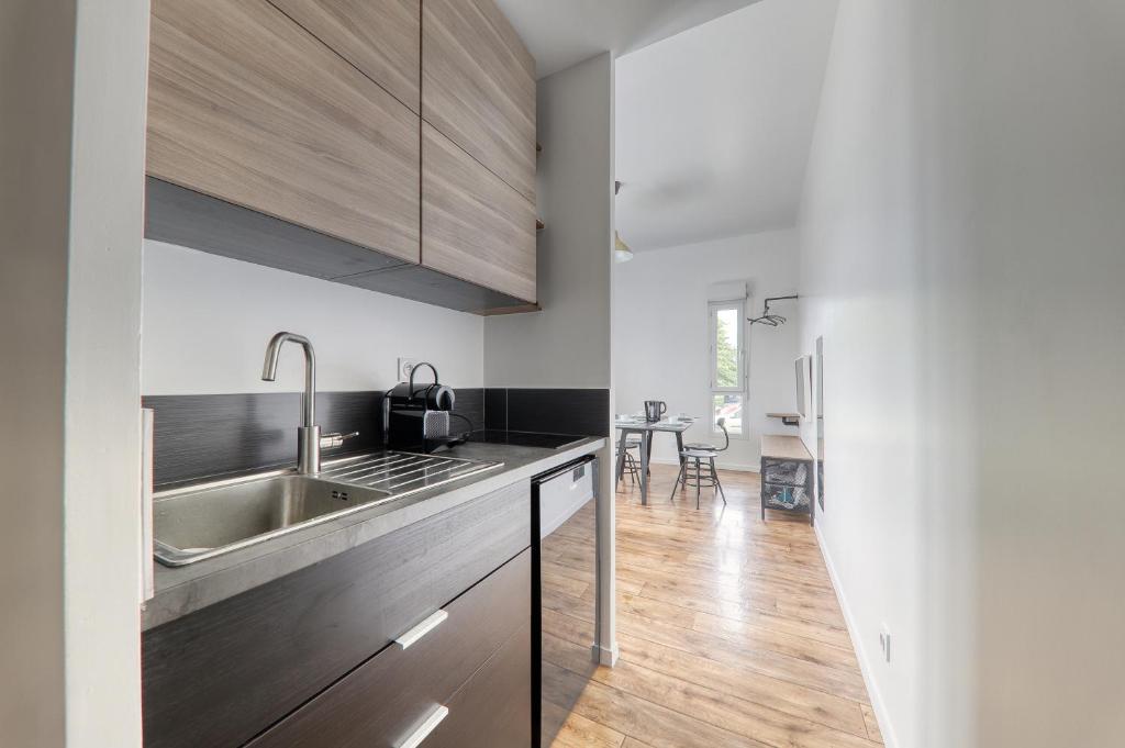 a kitchen with white walls and wooden cabinets at Studio Art - Shopping center and train station 500m - Disneyland Paris 5min in Montévrain