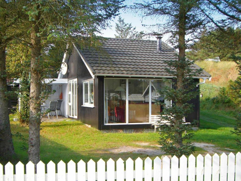 una piccola casa con una recinzione bianca di fronte di Two-Bedroom Holiday home in Blokhus 6 a Blokhus
