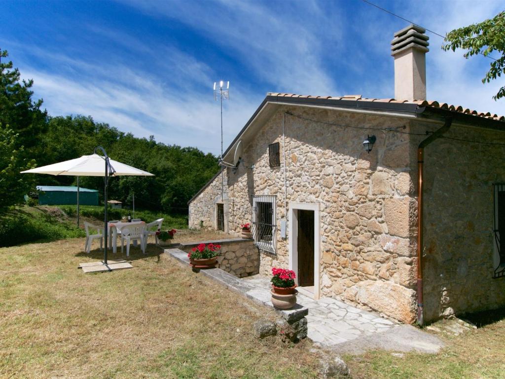 una pequeña casa de piedra con mesa y sombrilla en Val Giardino Vintage Cottage, en Roccamorice