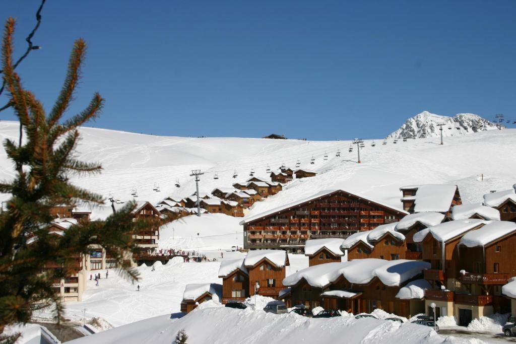 une station de ski avec des bâtiments recouverts de neige et une remontée mécanique dans l'établissement Madame Vacances Les Chalets du Praz, à La Plagne