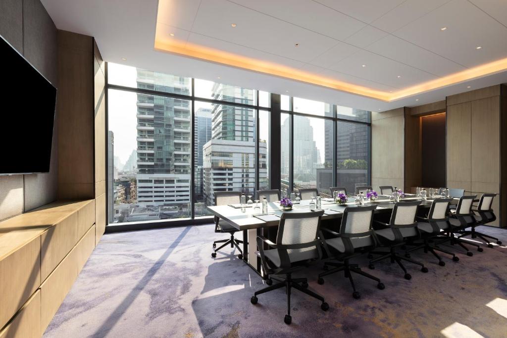A bright boardroom with a long meeting table, rolling chairs, wall-mounted display, and city views.