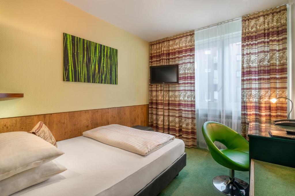 a bedroom with a bed and a green chair at Hotel Arosa Düsseldorf Oberkassel in Düsseldorf