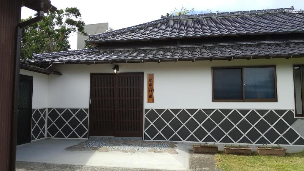 una casa en blanco y negro con una puerta marrón en 築100年の宿【はぶの家】, en Oshima