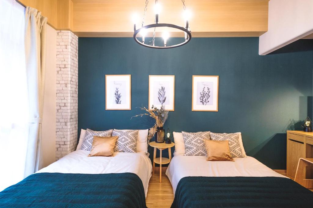2 Betten in einem Zimmer mit blauen Wänden und einem Kronleuchter in der Unterkunft Kuru Bentencho in Osaka