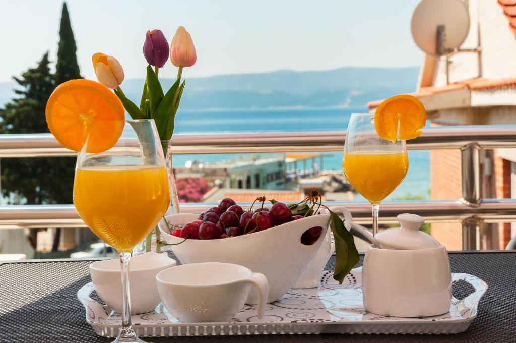 einen Tisch mit zwei Gläsern Orangensaft und einer Schale Obst in der Unterkunft Apartmani Joško Duće - Omiš in Duće