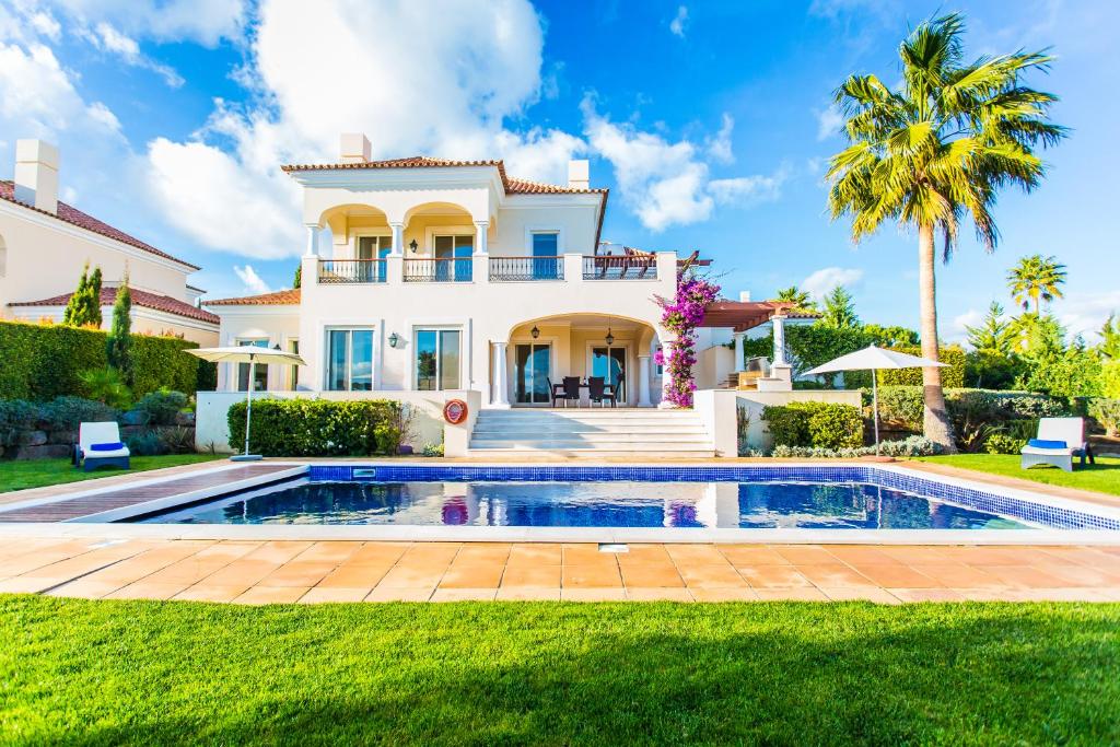 a villa with a swimming pool in front of a house at Monte Rei Golf & Country Club in Vila Nova de Cacela