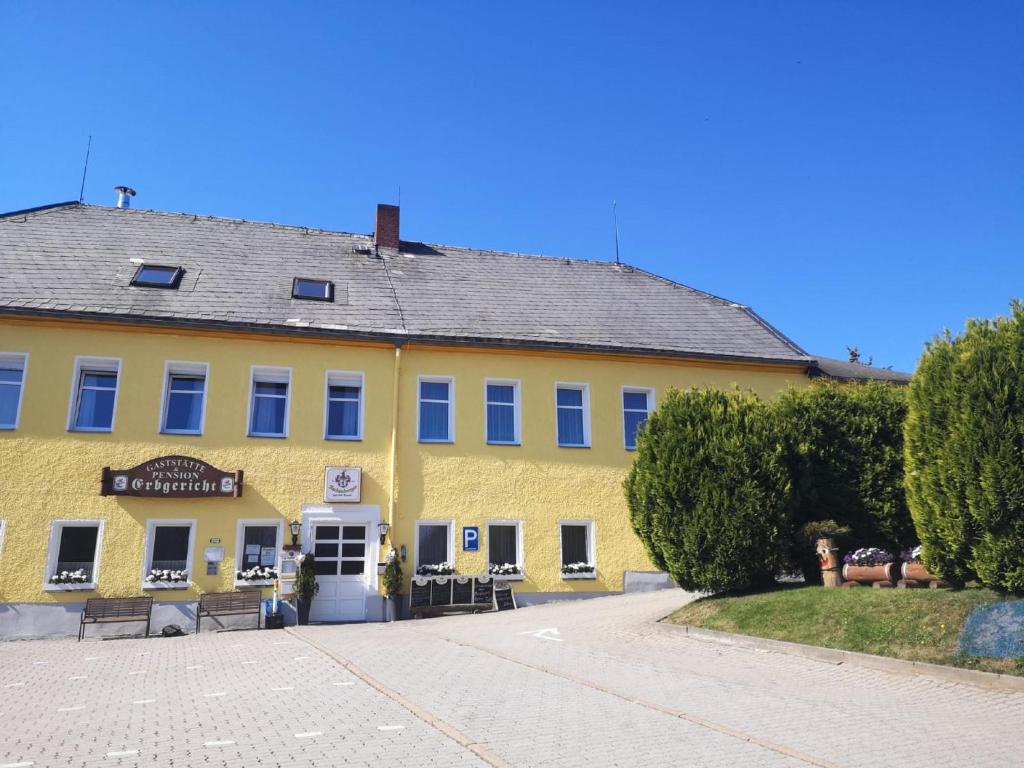 ein gelbes Gebäude mit einer Straße davor in der Unterkunft Pension & Gasthof Erbgericht Höhenlage 850m in Marienberg