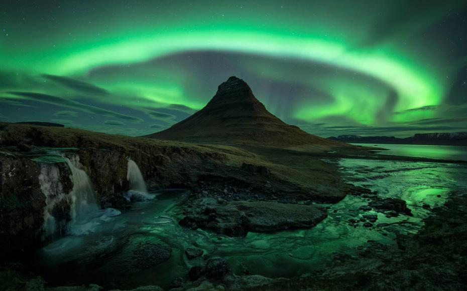 eine Aurora über einem Berg mit einem Fluss und einem Wasserfall in der Unterkunft Kirkjufell Guesthouse and Apartments in Grundarfjörður