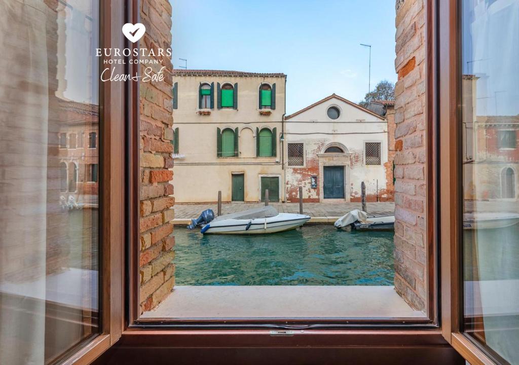 a window with a view of a canal with boats at Eurostars Residenza Cannaregio in Venice