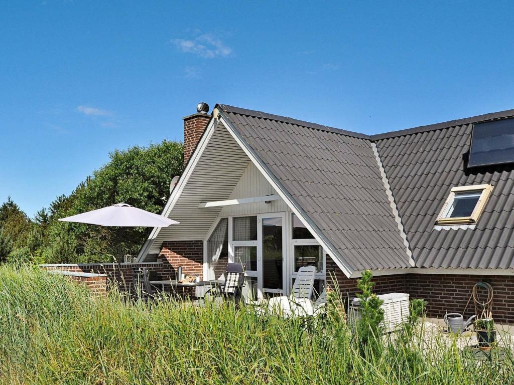 a house with chairs and an umbrella in front of it at 4 person holiday home in Ringk bing in Søndervig