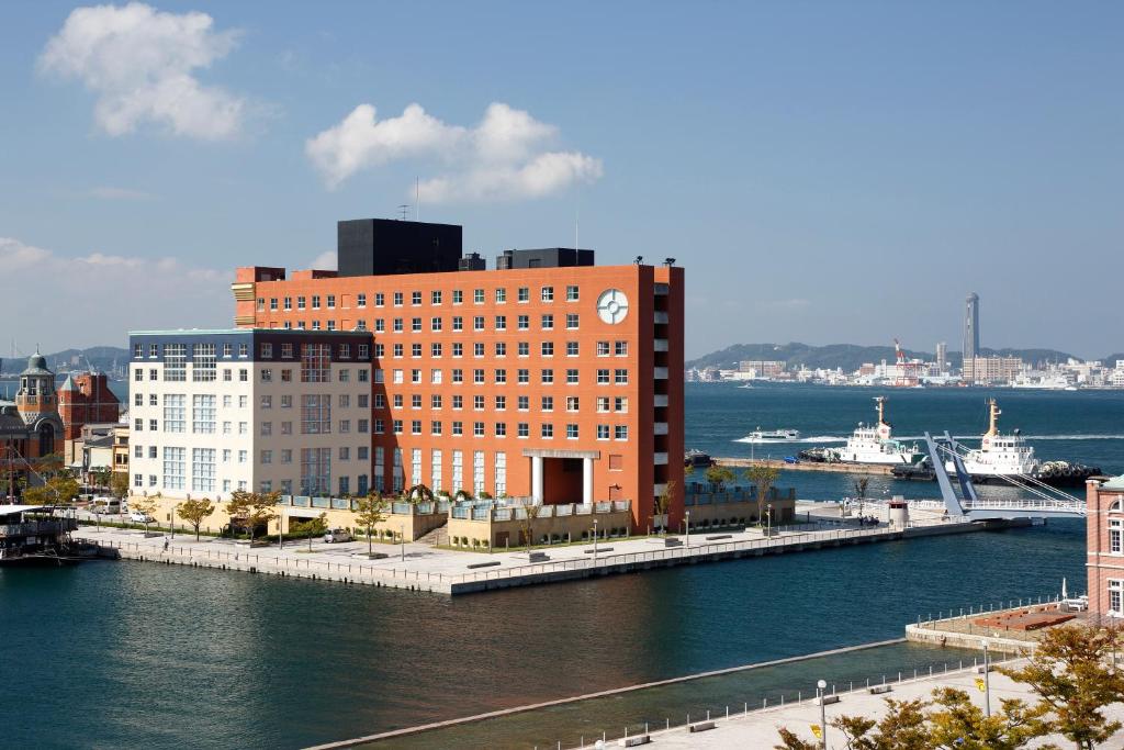Premier Hotel Mojiko في كيتاكيوشو: مبنى من الطوب كبير عليه ساعة بجانب الماء