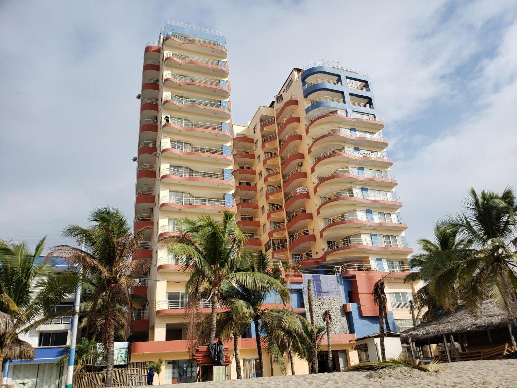 a tall building with palm trees in front of it at Arco Iris Atacames in Atacames