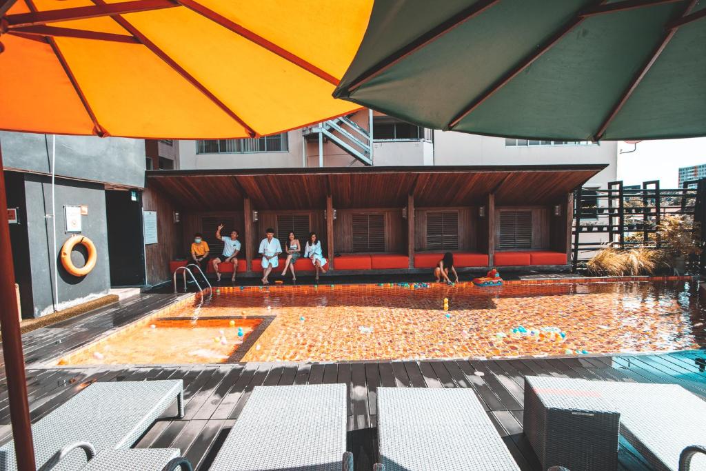 A colorful outdoor pool courtyard with loungers, umbrellas and a covered seating area.