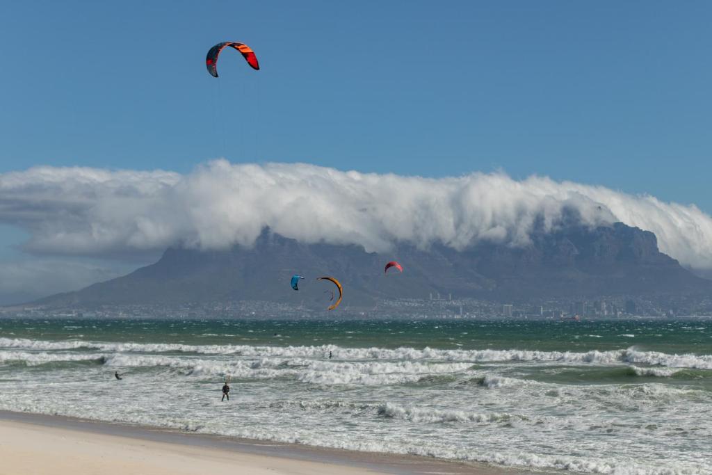 people flying kites on the beach with a mountain in the background at Blaauw Village Guest House in Bloubergstrand