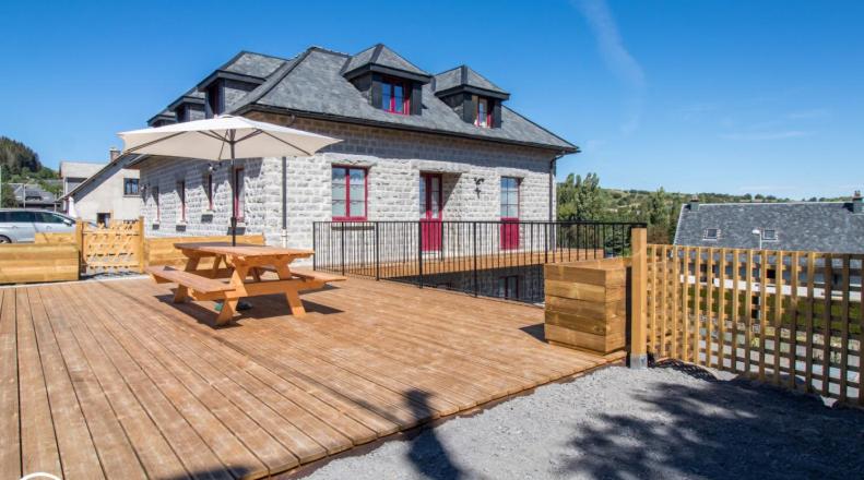 una terraza de madera con mesa de picnic y una casa en Gîte de Granit GRIS, en Besse-et-Saint-Anastaise