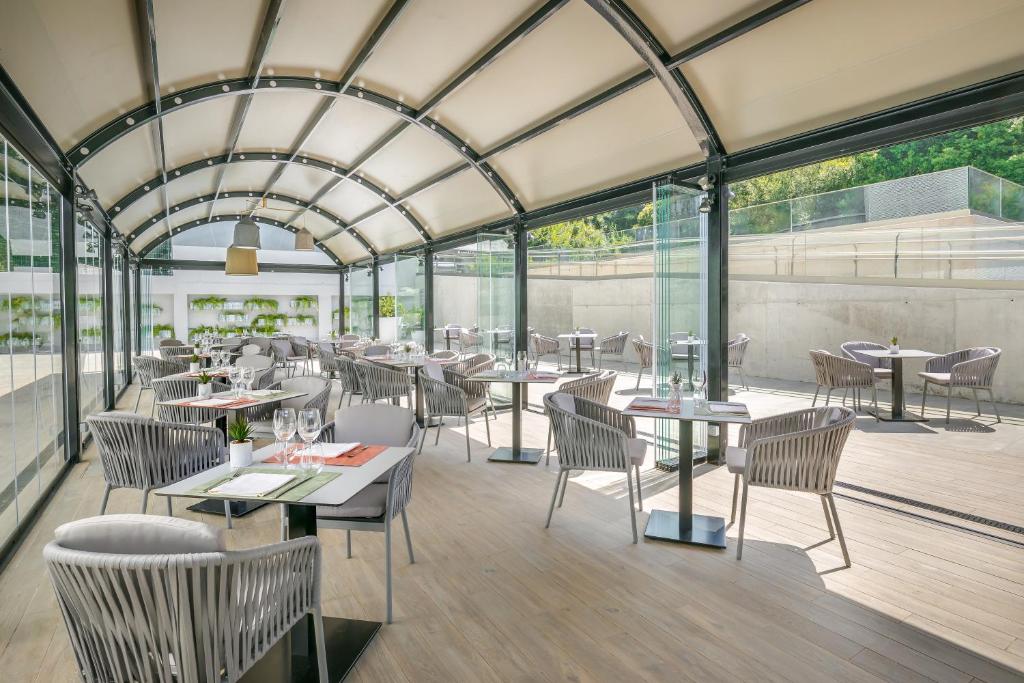 a restaurant with tables and chairs and glass walls at Barceló Costa Vasca in San Sebastián