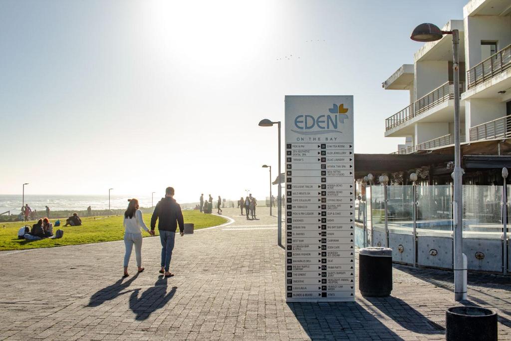 a man and woman walking down a sidewalk near a beach at Blaauw Village Guest House in Bloubergstrand