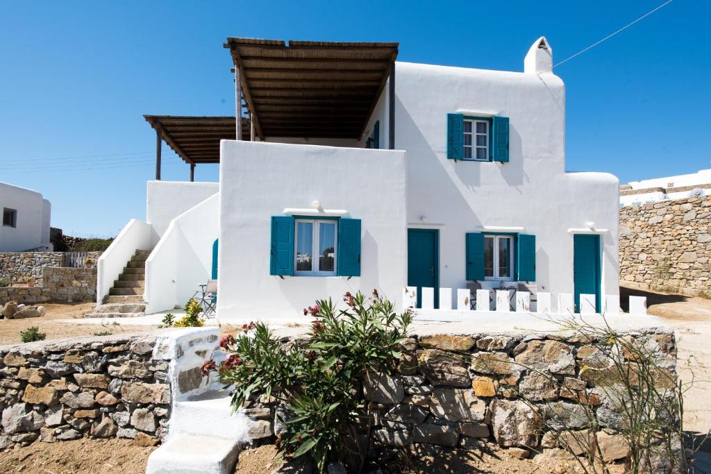 una casa bianca con finestre blu e un muro in pietra di A&A House Mykonos B ad Áno Merá