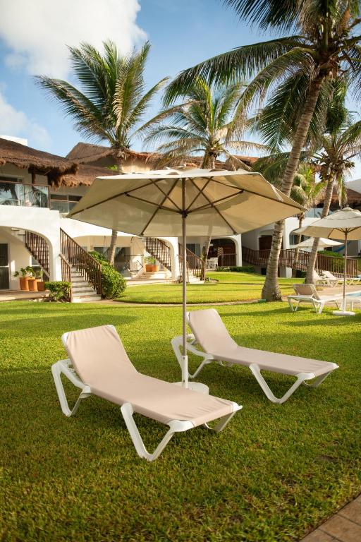 two lounge chairs and an umbrella on the grass at Las Villas Akumal in Akumal