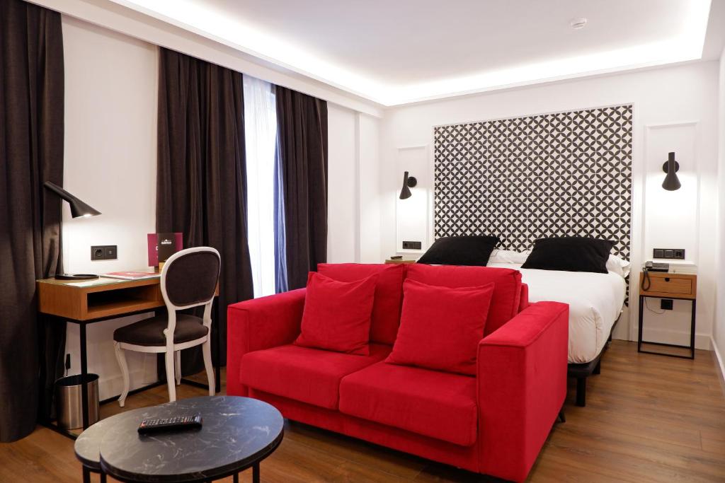 a hotel room with a red couch and a bed at Hotel Colón Plaza in Valladolid