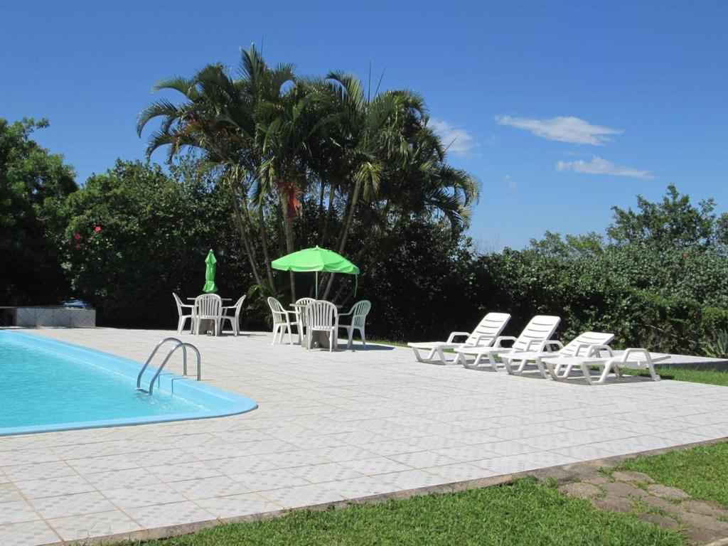 basen z krzesłami, stołem i zielonym parasolem w obiekcie Residencial Costa Esmeralda w mieście Florianópolis