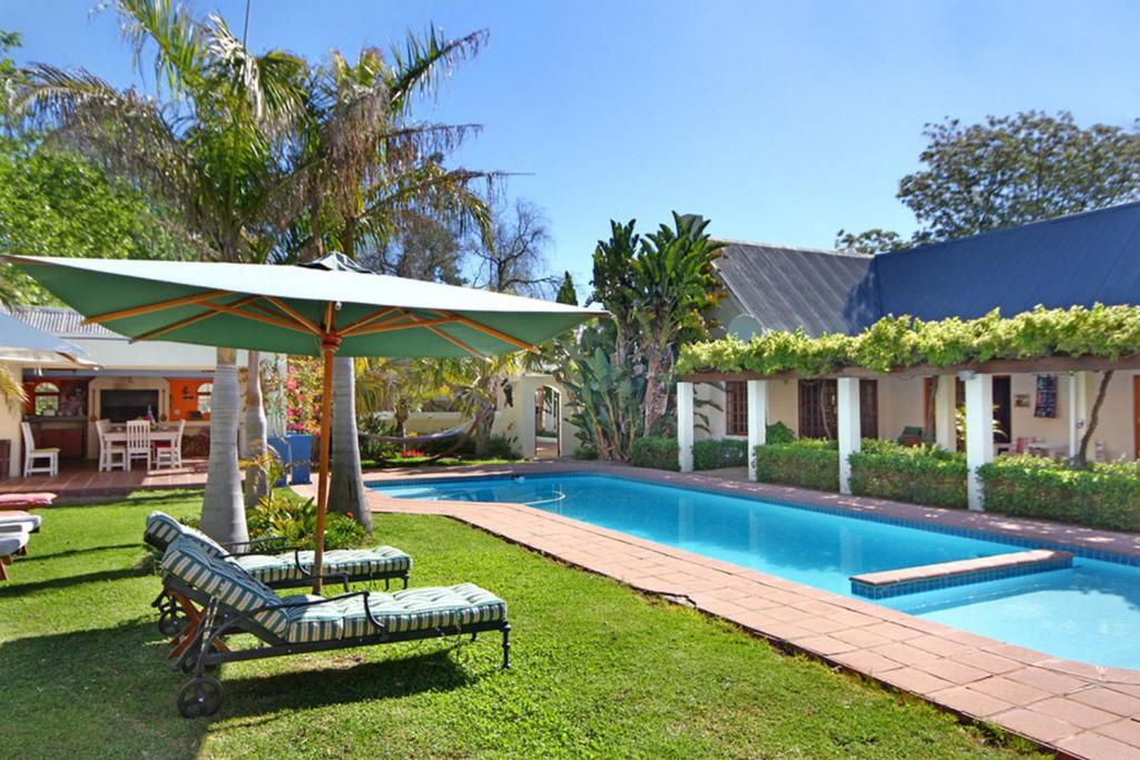 una piscina con 2 sillas y una sombrilla junto a una casa en Kleinbosch Lodge, en Stellenbosch