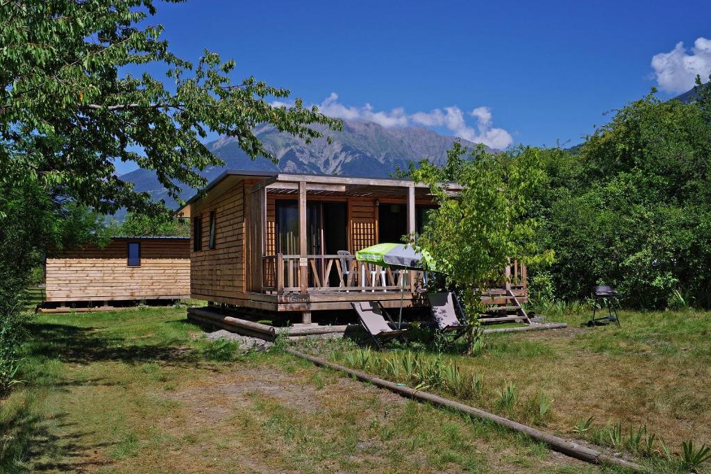 a small wooden cabin with a porch and an umbrella at Camping le Petit Liou Sites & Paysages in Baratier
