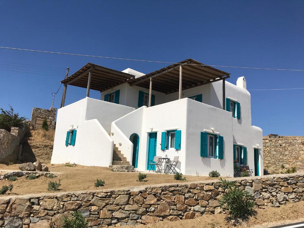a white house with blue shutters on a stone wall at A&A House Mykonos A in Ano Mera